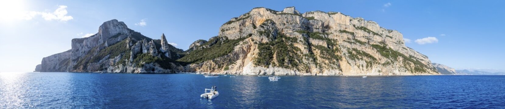 Couple on motorboat off picturesque rocky coast, cliffs with L'Aguglia pinnacle, blue sea and Cala Goloritz&eacute; beach, aerial view, Golfo di Orosei, Baunei, Sardinia, Italy