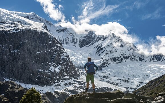 Mountaineer stands on rocks, impressive view of Rob Roy Glacier, Mount Aspiring National Park, Otago, South Island, New Zealand