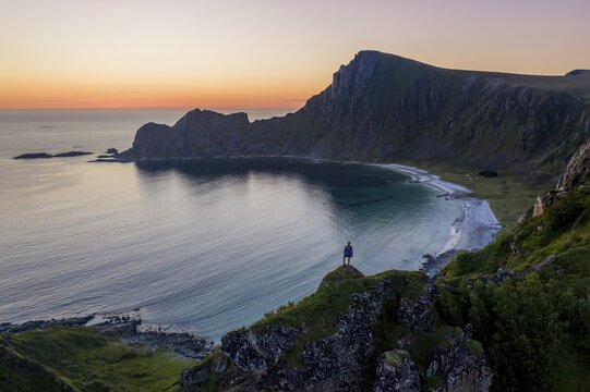 Evening mood, hiker on rocks, cliffs, beach and sea, in the back summit of the mountain M&aring;tinden, near Stave, Nordland, Norway