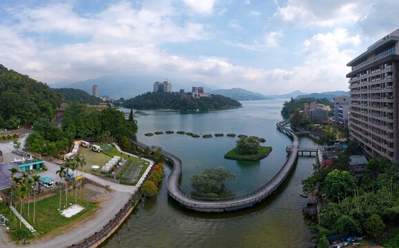 Aerial view of round-the-lake bikeway winding above the water and along the shoreline with high-rise hotels standing on the green wooded hills by Sun Moon Lake, a famous tourist destination in Taiwan