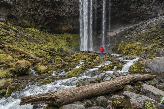 Young woman, hiker stands in front of a high waterfall, water falls down, Tamanawas Falls, Wild River Cold Spring Creek, Oregon, USA