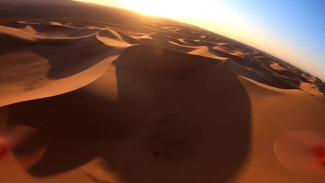 Vast expanse of golden sand dunes in a desert landscape at sunset with the sun casting long shadows and a clear sky overhead