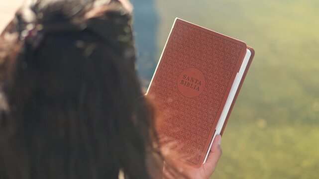 Over-the-shoulder view of woman holding a Spanish Holy Bible in a park