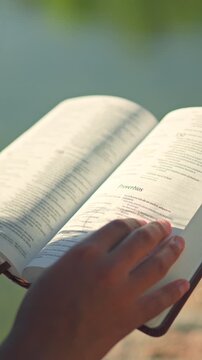Hand turning pages of open Spanish Holy Bible in sunlight
