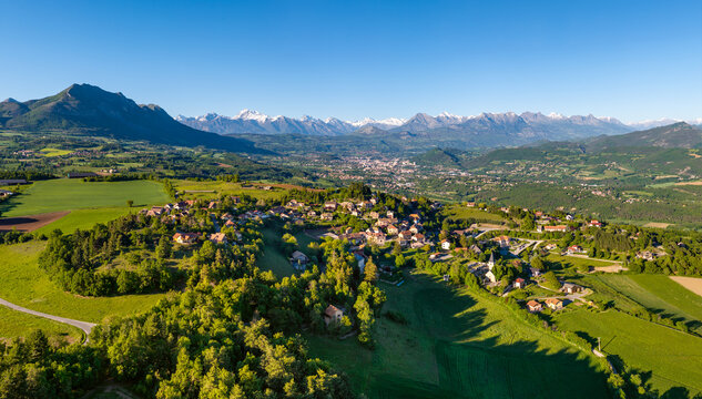 Aerial summer view of Pelleautier village with view of the city of Gap (capital of Hautes-Alpes department) with Champsaur and Ecrins Massif mountain peaks in the distance. France