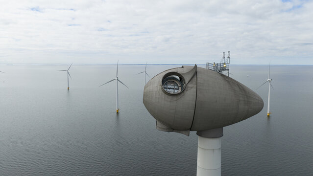Aerial view of an offshore wind turbine nacelle with a maintenance platform, surrounded by other wind turbines in the water under a cloudy sky in Espel, Flevoland, Netherlands.