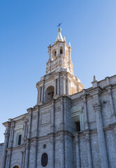 Fototapeta premium The intricate white sillar stone facade and bell tower of the historic Basilica Cathedral of Arequipa stand tall against a clear blue sky in Arequipa, Peru.