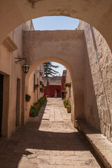 Naklejka premium A perspective view through historic white sillar stone arches reveals a cobblestone street lined with potted geraniums and leading toward vibrant red buildings within Santa Catalina Monastery in Arequ