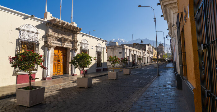 Historic sillar stone buildings line a colonial street leading toward the bell tower and facade of the San Francisco Church in Arequipa, Peru
