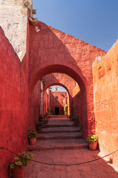 A symmetrical view looking up a stone staircase framed by multiple red sillar archways, leading toward a historic bell gable under a clear blue sky at Santa Catalina Monastery in Arequipa, Peru.