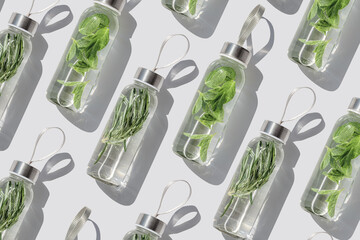 Fresh water refreshing detox drink in glass bottle at sunlight on white background. Top view bottles of infusing water with green aromatic spicy herbs. Healthy lifestyle, minimal creative pattern. © yrabota