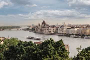 Fototapeta premium High angle scenic view of the Hungarian Parliament Building and Danube river with a cruise ship framed by green trees in Budapest