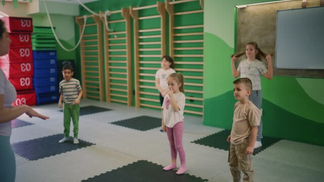 Children enthusiastically perform jumping jacks with their instructor in a group fitness class. This vibrant indoor exercise session promotes active and healthy lifestyles for kids.