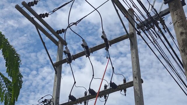 Low angle video of operating an insulated hot stick tool to disconnect high voltage drop out fuse cutouts phase by phase on a concrete power transformer pole structure against a blue sky.