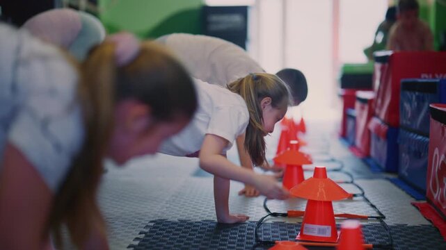 Children are actively engaged in fitness training, navigating agility ladders and cones on the gym floor. Young athletes perform dynamic exercises in an indoor sports facility.
