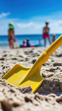 Yellow toy shovel on sandy beach with blurred kids