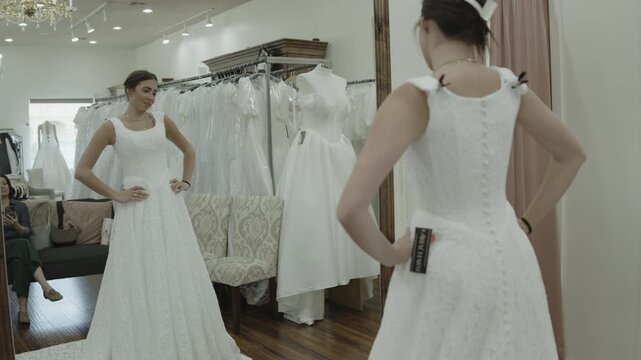 A young woman is trying on wedding dresses while her mother observes in the background, St. George, Utah