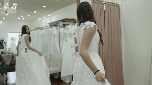 A young woman is trying on wedding dresses while her mother observes in the background, St. George, Utah
