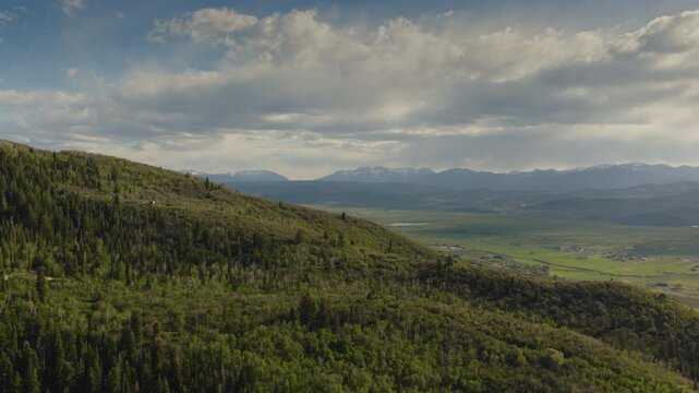 An aerial flyover of foothills near the Uintah mountains revealing a valley and farmland in the distance, Kamas, Utah