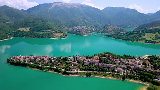 Colle di Tora medieval borgo peninsula drone view Lago del Turano Lazio Italy. Cinematic smooth turn over turquoise lake calm water surface, green hills scenic village landscape 4K.