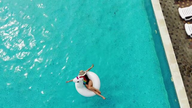 Beautiful woman on unicorn pool float in pool. Summer holidays. Aerial top view from drone
