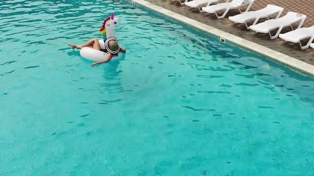 Beautiful woman on unicorn pool float in pool. Summer holidays. Aerial top view from drone
