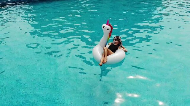 Beautiful woman on unicorn pool float in pool. Summer holidays. Aerial top view from drone
