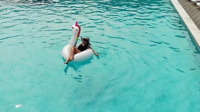 Beautiful woman on unicorn pool float in pool. Summer holidays. Aerial top view from drone
