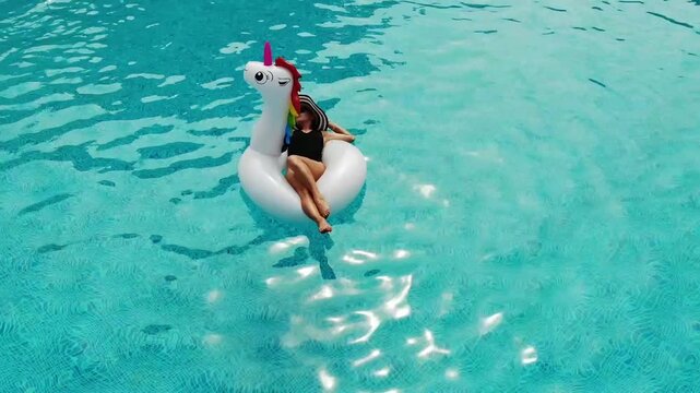Beautiful woman on unicorn pool float in pool. Summer holidays. Aerial top view from drone
