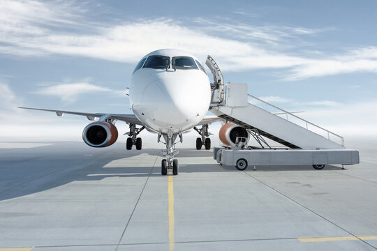 Front view of the white passenger airliner with boarding steps isolated on bright background with sky