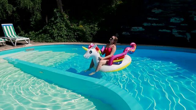 Woman on inflatable unicorn pool float in pool in hotel. Summer holidays, enjoying summer vacations 
