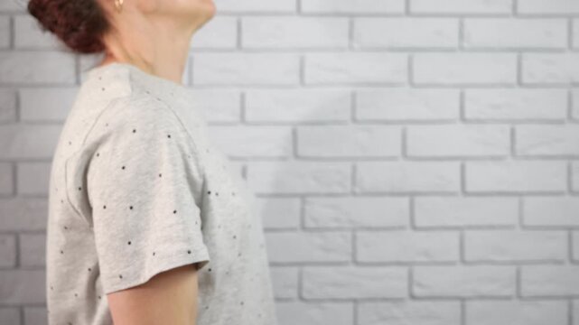 Strength training at home. Athletic woman performing bicep curls with a heavy dumbbell during a workout session, building muscle strength in a home gym against a white brick wall background