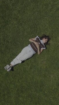 An aerial flyover vertical video of a young woman asleep, laying on the grass in a park, St. George, Utah