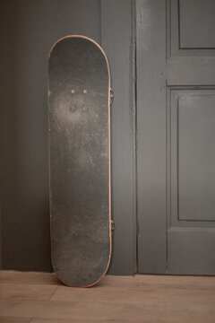 Black skateboard leaning against a dark wall indoors, urban sport gear, youth lifestyle, casual recreation, minimalist interior.