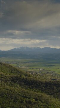 An aerial flyover vertical video of foothills near the Uintah mountains revealing a valley and farmland in the distance, Kamas, Utah