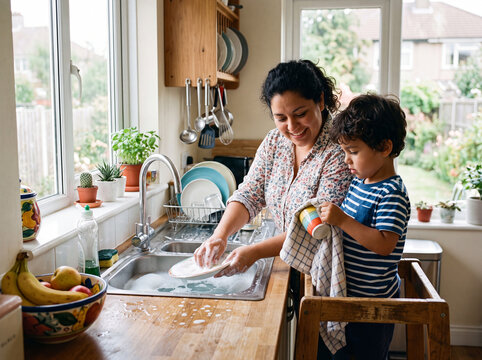Latin mother teaching her young son to wash dishes at home