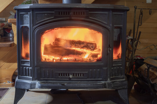 Burning firewood inside a cast iron stove creating comfortable warmth for home heating. Cozy winter interior with natural wood fuel.