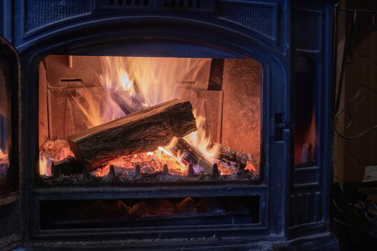 Burning firewood inside a cast iron stove creating comfortable warmth for home heating. Cozy winter interior with natural wood fuel.