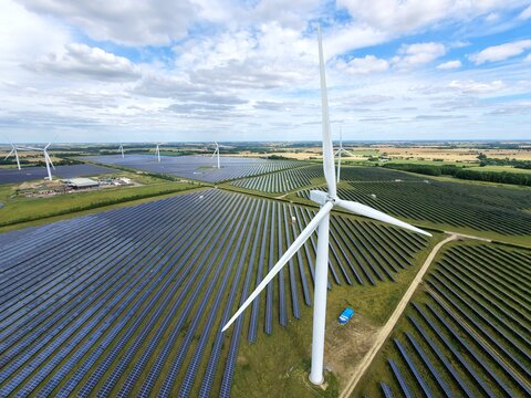 Aerial view of Chelveston Renewable Energy featuring wind turbines and rows of solar panels in a rural landscape under a cloudy sky in Chelveston, England, United Kingdom.