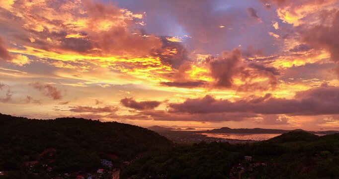 A breathtaking aerial panoramic view of a vibrant golden sunset illuminating the sky above a lush green hilltop with a small structure, surrounded by scattered clouds and distant landscapes.