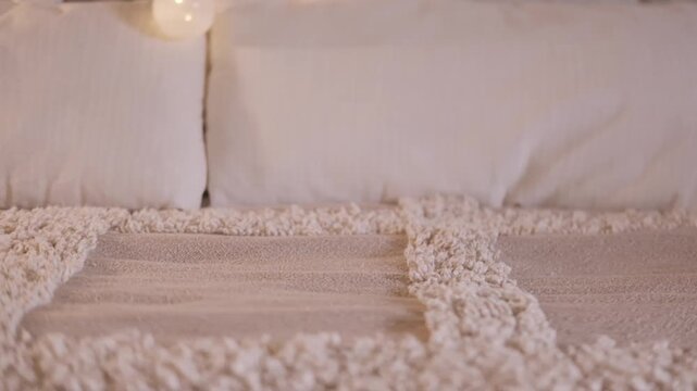 Bed with unlit decorative fairy lights in bedroom, soft beige blanket with white pillows, decorated brick wall and glowing string lights in background, cozy calm home atmosphere, Evening relaxation