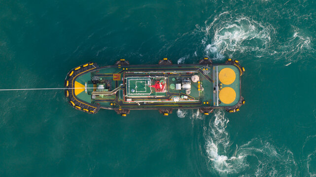 Aerial view of a tugboat navigating through the turquoise waters of the port, creating a wake in Laem Chabang, Chon Buri, Thailand.