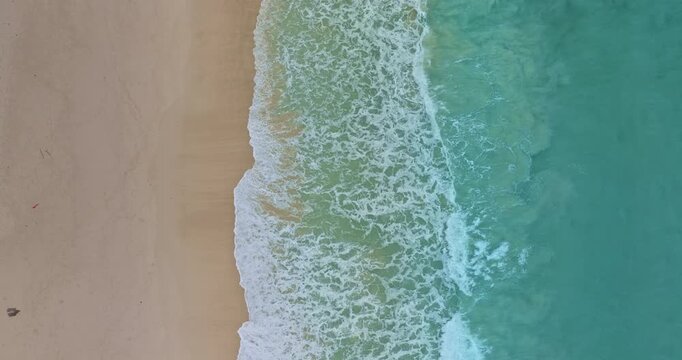 aerial top view The waves slowly swept towards the shore.
White foam waves in the bright green sea lapping on the white sandy beach.
white bubble waves, and clear sand landscape. freedom beach.