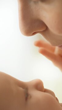A mother sits with her baby, letting the infant press a fingertip to her lips while the child looks up and gently touches her face with a hand, daily maternal care in a family setting