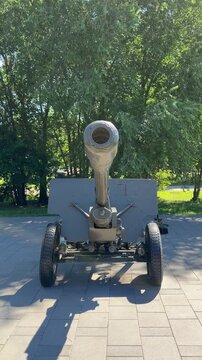 Antique Artillery Piece: A vintage cannon, a relic of past conflicts, stands on a paved surface surrounded by lush greenery and trees, casting a long shadow.