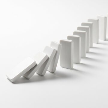Minimalist white dominoes falling in a row, chain reaction concept on bright background, sequence of falling blocks representing cause and effect