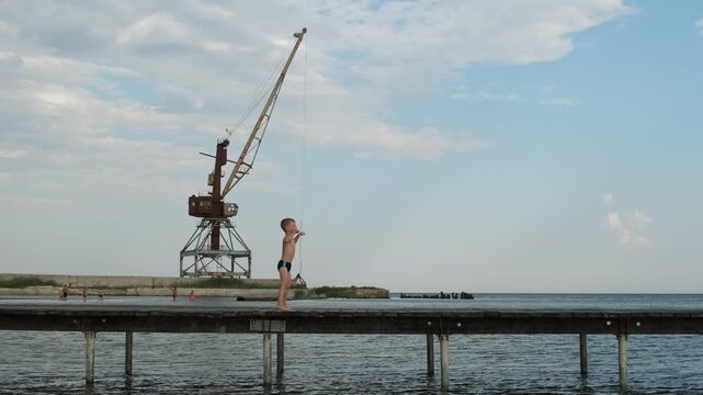 Funny little boy dancing hip hop and posing on a wooden pier near the sea with a crane background