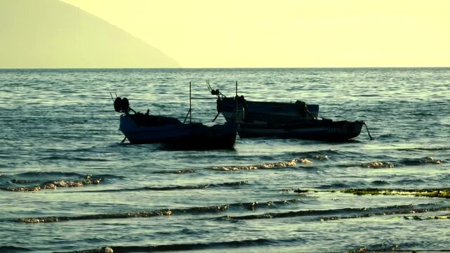 Wooden Fishing Boats Anchored In Shallow Sea Water During.  Rippling Waves And  Mountain At Dawn