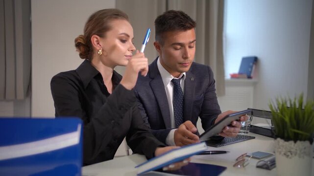 Office team working together on business project, man showing tablet to woman colleague, both discussing content, man looks off-camera but no one enters frame.
