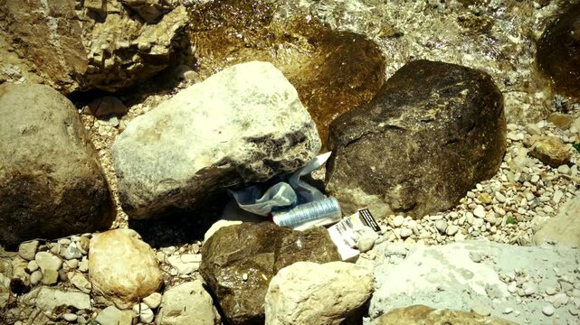 Plastic Trash And Aluminum Can Left Discarded Among Rocks On Pebble Shore. Environmental Pollution. Ecology Issue In Nature 
